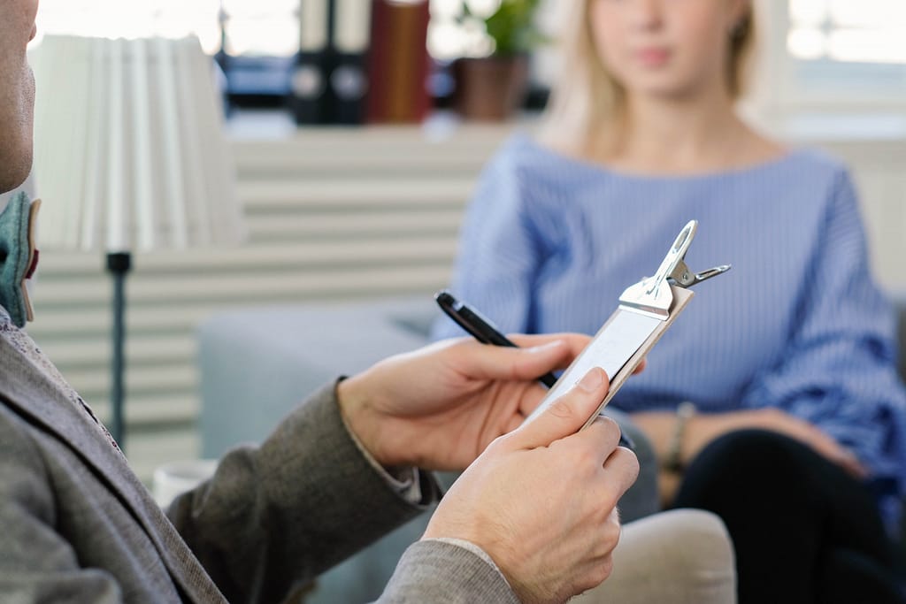 A mental health professional holding a clipboard and pen, preparing to document notes during a therapy session. This setting represents the use of the 90839 CPT Code for billing extended crisis therapy sessions.