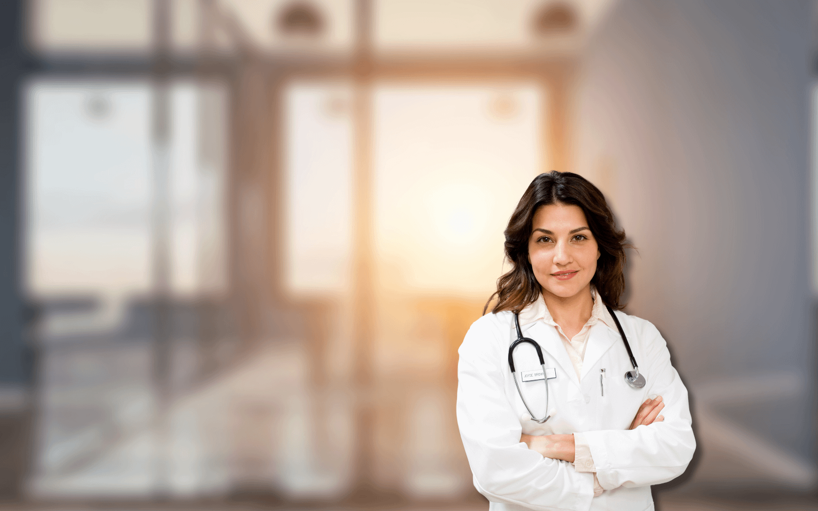 A confident doctor in a white coat with a stethoscope, standing with arms crossed in a modern hospital, representing the F10.20 ICD-10 code guide for medical coders and billers. The blurred background with warm lighting highlights a professional healthcare setting