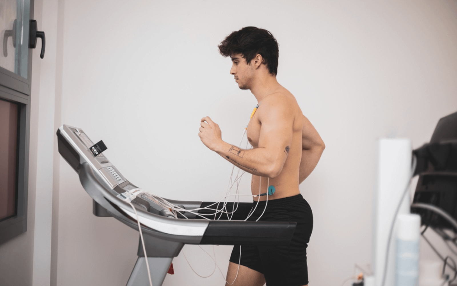 A man running on a treadmill with electrodes on his chest for stress testing, monitoring heart activity in a clinical setting.